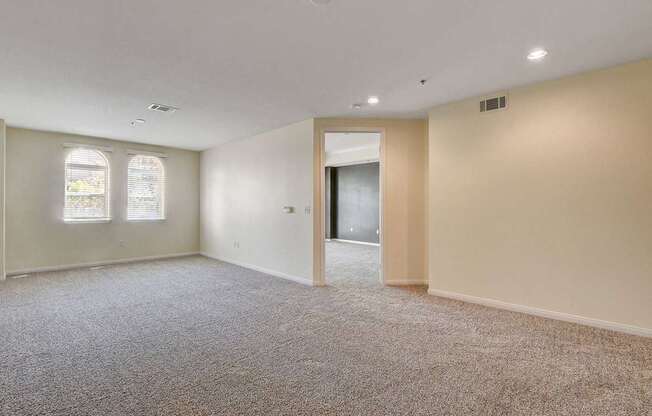 A large empty room with carpeted floor and two windows.