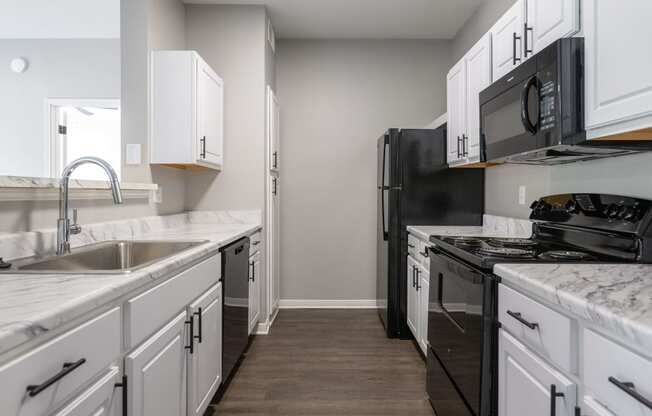 an empty kitchen with white cabinets and black appliances and a sink