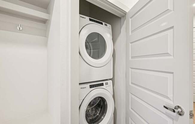 A white washing machine is in a cabinet under a white door.