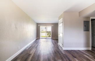 an empty living room with wood flooring and a door to a balcony