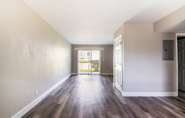 an empty living room with wood flooring and a door to a balcony