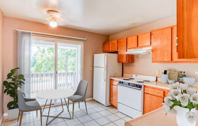 A simple kitchen with wooden cabinets, a white refrigerator, stove, microwave, and dishwasher on tiled flooring.