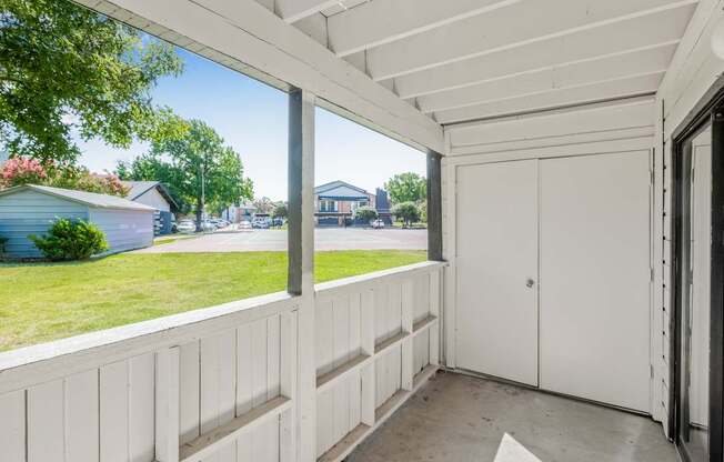 A white wooden balcony with a white door and a window overlooking a green lawn and a blue house.