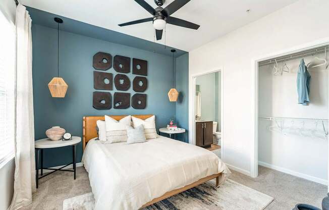 A bedroom with a bed, a ceiling fan, and a wall hanging.
