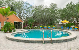 a swimming pool with blue and yellow chaise lounge chairs and trees in the background