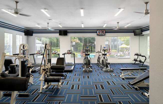 a gym with cardio machines and weights in a room with windows