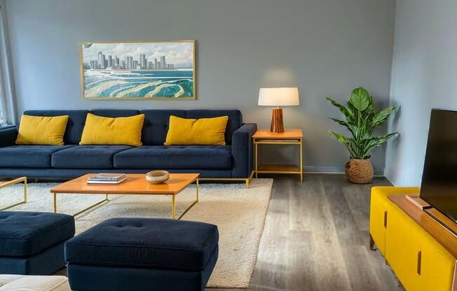 A living room with a blue couch, yellow pillows, and a painting on the wall.