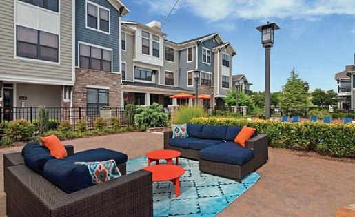 outdoor living room with modern seating next to lush landscaping and apartment buildings