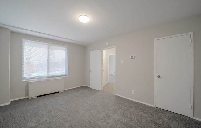A room with a carpeted floor, a window with blinds, and a ceiling light.