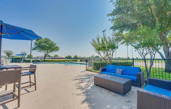 A pool area with a blue umbrella and a brown wicker chair.