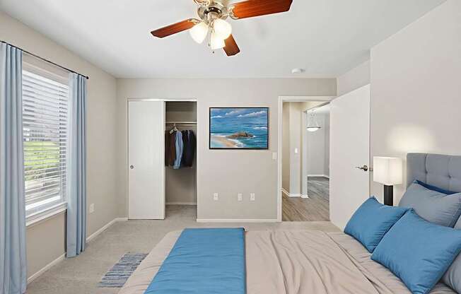 A bedroom with a bed, a ceiling fan, and a painting of a beach scene on the wall.