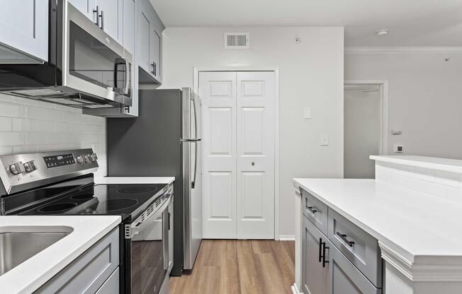 Modern kitchen featuring stainless steel appliances including a microwave, oven, and refrigerator. The cabinetry is a mix of light and dark tones, with a white countertop and a stylish backsplash. The space has wooden flooring and white walls, creating a bright and inviting atmosphere.