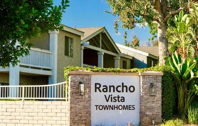 A sign for Rancho Vista Townhomes in front of apartment homes with balconies and lush green landscaping.