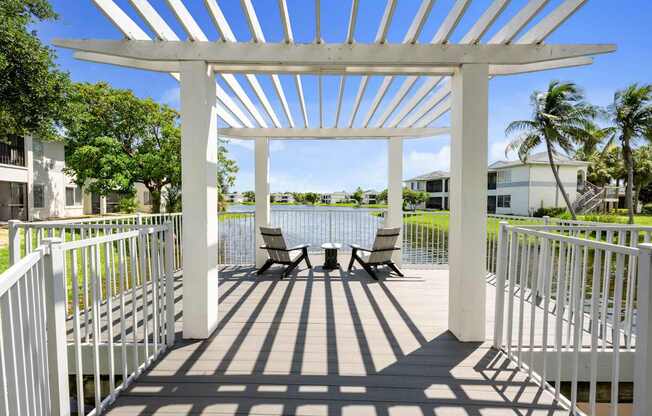 a patio with a pergola and chairs overlooking a body of water