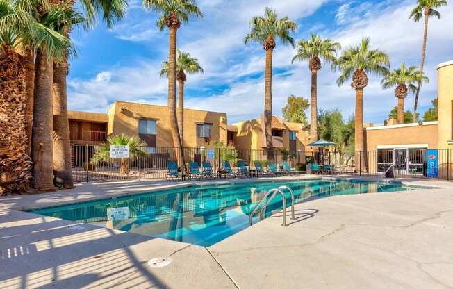 A pool surrounded by palm trees and a building in the background.