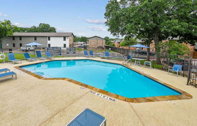 A large swimming pool surrounded by a fence and lounge chairs.