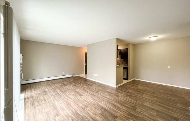 an empty living room with hardwood floors and a kitchen in the background