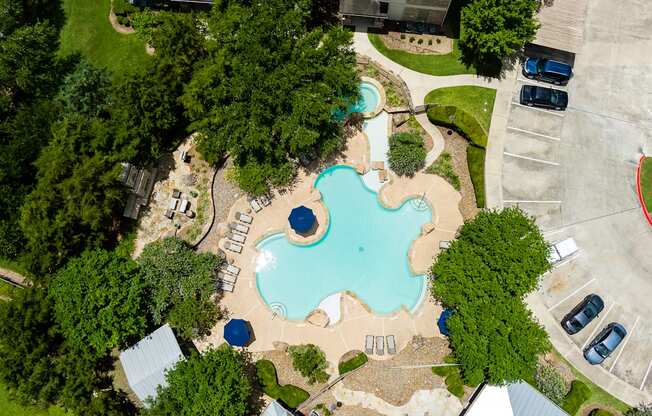 A large swimming pool surrounded by trees and a parking lot.