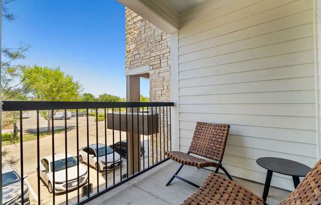 A balcony with a table and two chairs overlooks a parking lot.