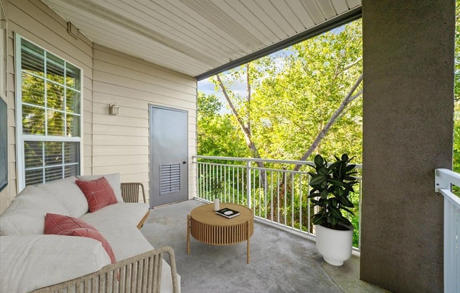 A patio with a couch, table, and potted plant.
