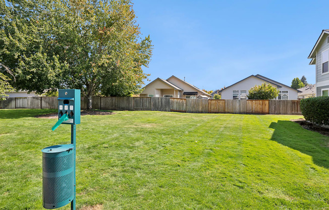 A green trash can sits in a grassy yard.