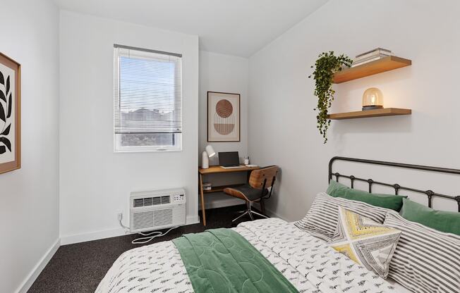 A bedroom with a bed, desk, and window.