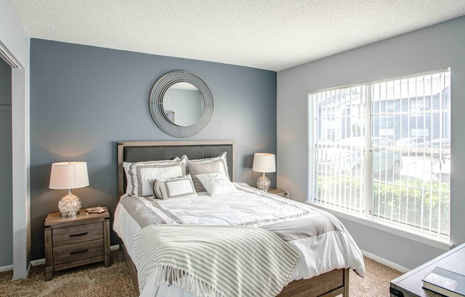 A bedroom with a large bed, two nightstands, and a round mirror on the wall.