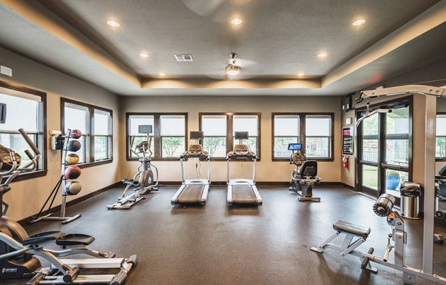 a gym with cardio machines and weights on the floor and windows