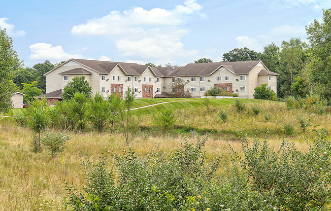 A large house with a grey roof and red doors is surrounded by greenery.