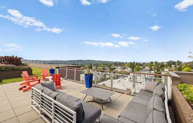 A patio with grey couches and red chairs overlooks a cityscape.