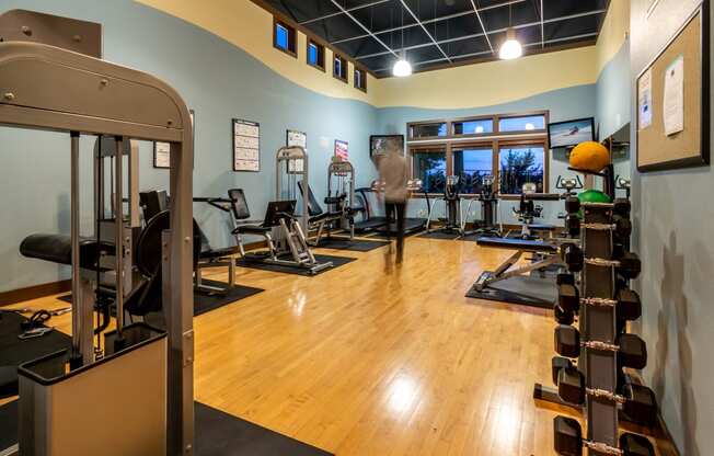 a spacious fitness room with cardio equipment and a man working out in the background