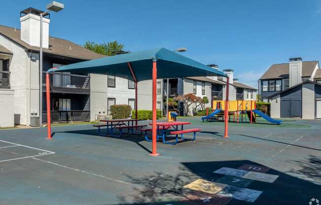an outdoor playground with a picnic table and swing set in front of apartments