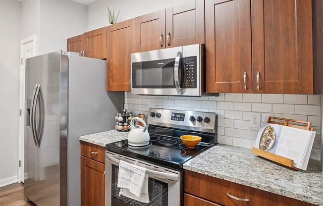 A kitchen with a refrigerator, microwave, oven, and a stove top.