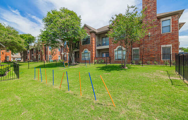 A grassy area in front of a brick building with orange and blue poles sticking out of the ground.