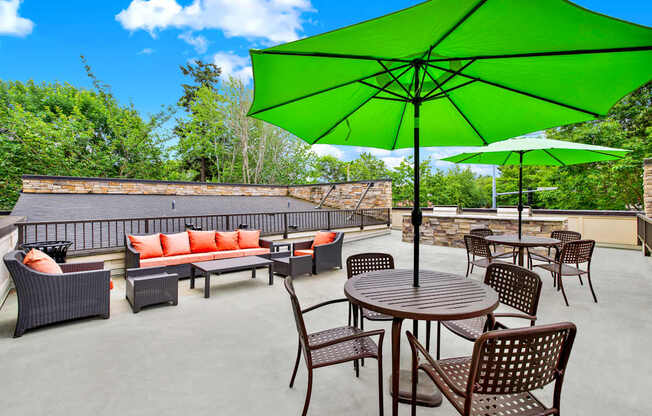 A patio with a green umbrella and brown furniture.