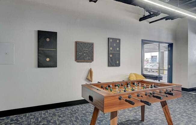 A foosball table is in the middle of a room with a white wall and a window.