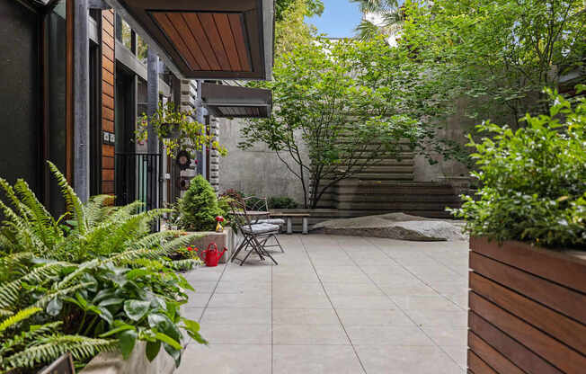 A patio with a table and chairs surrounded by green plants.