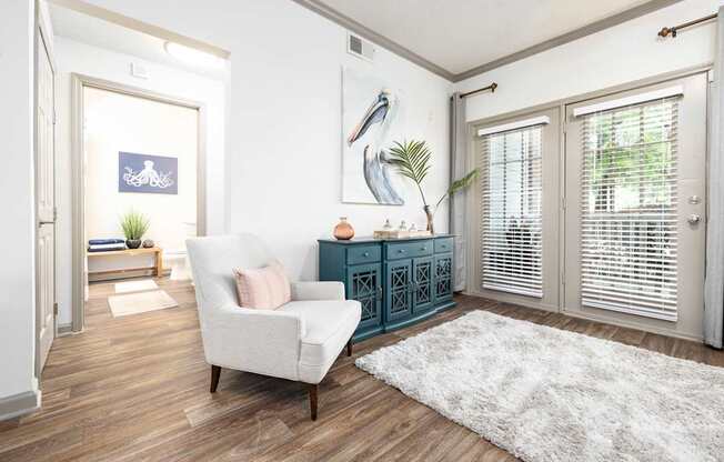 A white chair is in front of a cabinet and a painting of a bird at The Palms at Chatham apartments in Savannah GA.