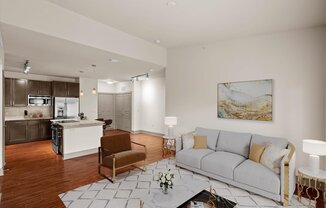 a living room with a couch and a chair in front of a kitchen with a stove and