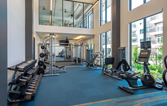 a gym with cardio machines and weights in a building with large windows