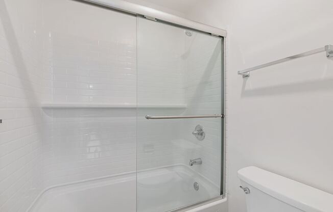 A white bathroom with a glass shower door and a white bathtub.