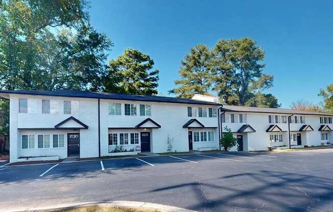 A white building with black trim and windows is surrounded by trees.