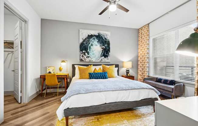 A bedroom with a bed, a chair, a painting, and a ceiling fan.