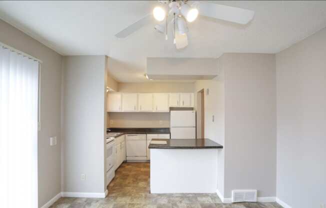 an empty kitchen with white cabinets and a ceiling fan