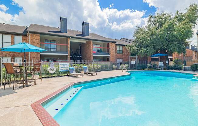 A large swimming pool in front of a building with a blue sky and clouds in the background.