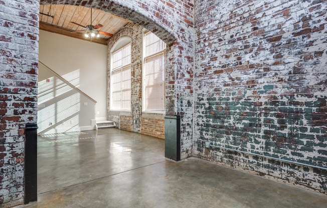 View of Living Room, Showing View of Stairway, Historic Mill Bricks for Walls, and Ceiling Fan at Alpha Mill Apartments