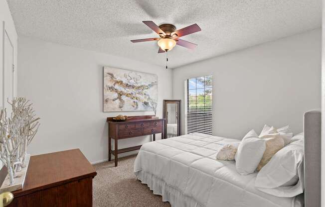 A bedroom with a bed, dresser, and a ceiling fan.