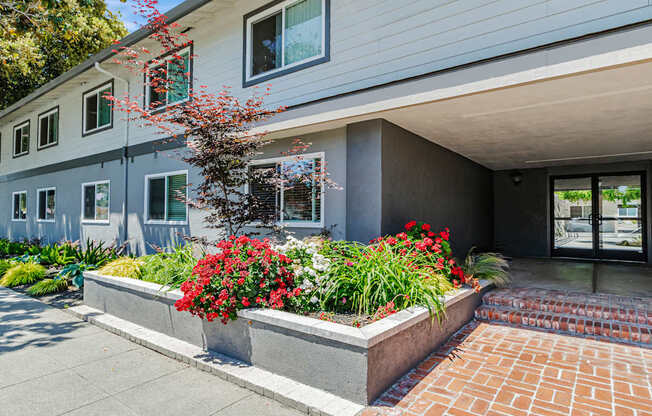 A modern building with a grey exterior and a red brick walkway leading to the entrance.