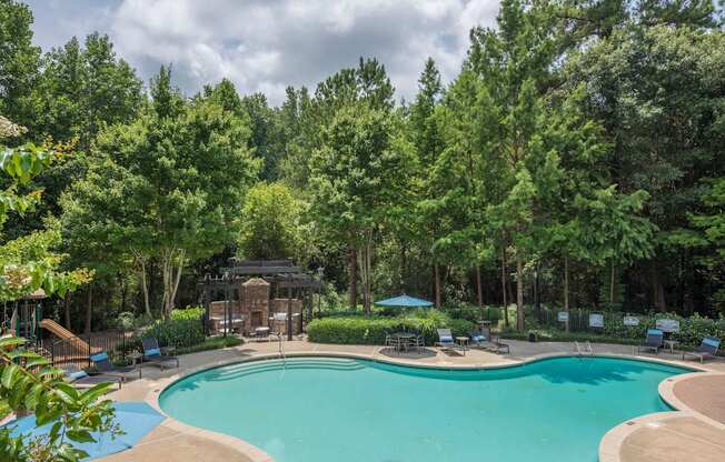 a swimming pool with chairs around it and trees in the background