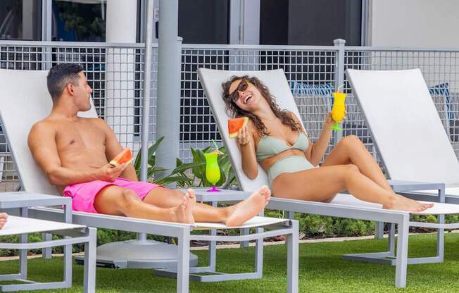 A man and a woman are sitting on lounge chairs outside, enjoying drinks and watermelon.at Icon One, Daytona Beach